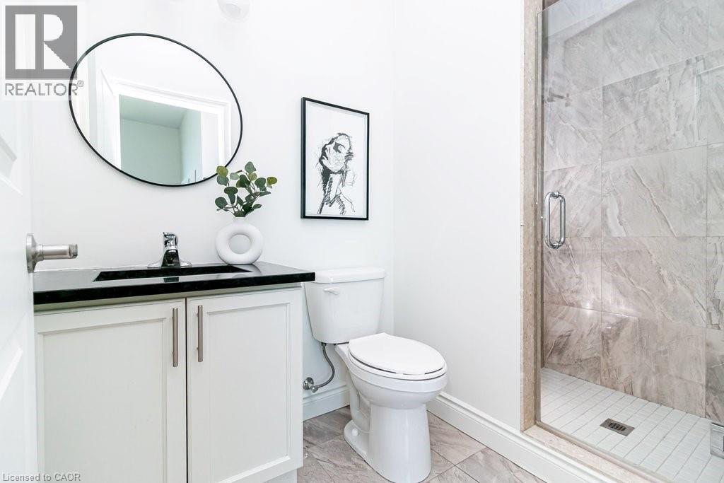 Bathroom featuring a glass-enclosed shower with large-format stone-look tile, white vanity with dual doors and brushed nickel hardware, black countertop, and a circular mirror - 101 Shoreview Place Unit# 631, Stoney Creek, ON - Indoor Photo Showing Bathroom