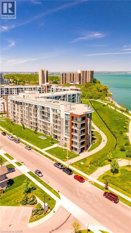 Modern multi-story building featuring balconies, a prominent waterfront setting, curved pedestrian pathways, and manicured green spaces - 101 Shoreview Place Unit# 631, Stoney Creek, ON - Outdoor With Body Of Water With View