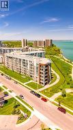 Modern multi-story building featuring balconies, a prominent waterfront setting, curved pedestrian pathways, and manicured green spaces -