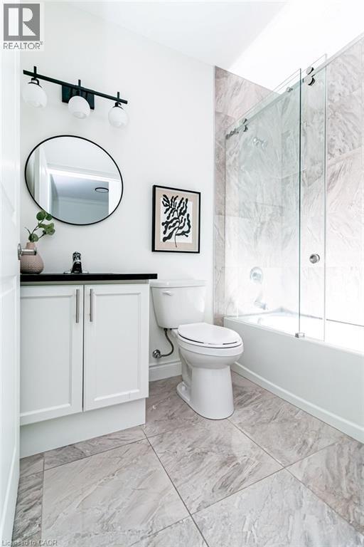 Contemporary bathroom featuring a white vanity with black countertop, a round mirror, and a three-light matte black fixture - 101 Shoreview Place Unit# 631, Stoney Creek, ON - Indoor Photo Showing Bathroom