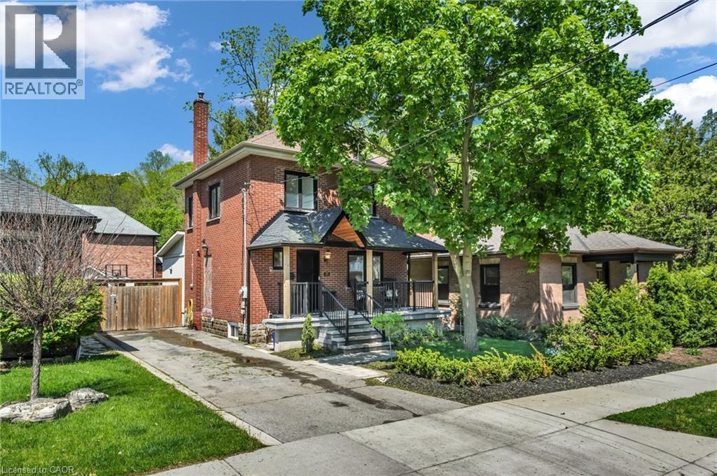 Brick exterior with a prominent chimney and a covered front porch featuring black railings - 25 Park Street E, Hamilton, ON - Outdoor