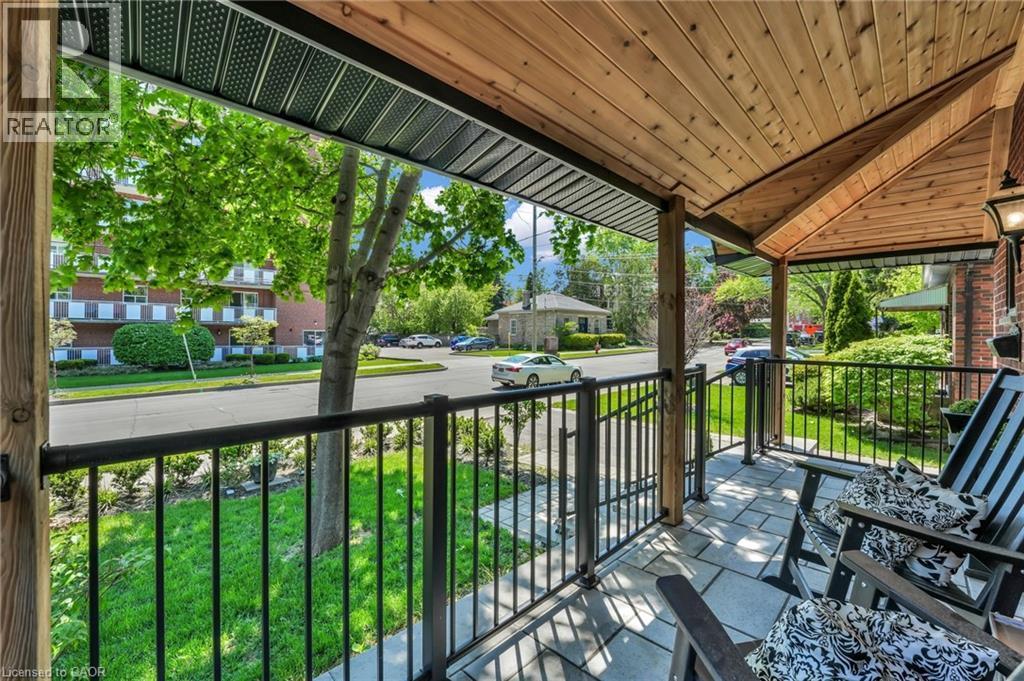 Covered front porch featuring a natural wood-finish ceiling, dark metal railings, square paver flooring, and exposed wood support posts - 25 Park Street E, Hamilton, ON - Outdoor With Deck Patio Veranda With Exterior