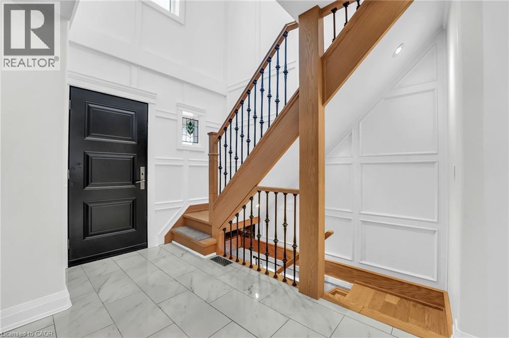 Foyer featuring a black paneled entry door, light wood staircase with wrought iron balusters, white wainscoting, and large format tile flooring - 25 Park Street E, Hamilton, ON - Indoor Photo Showing Other Room