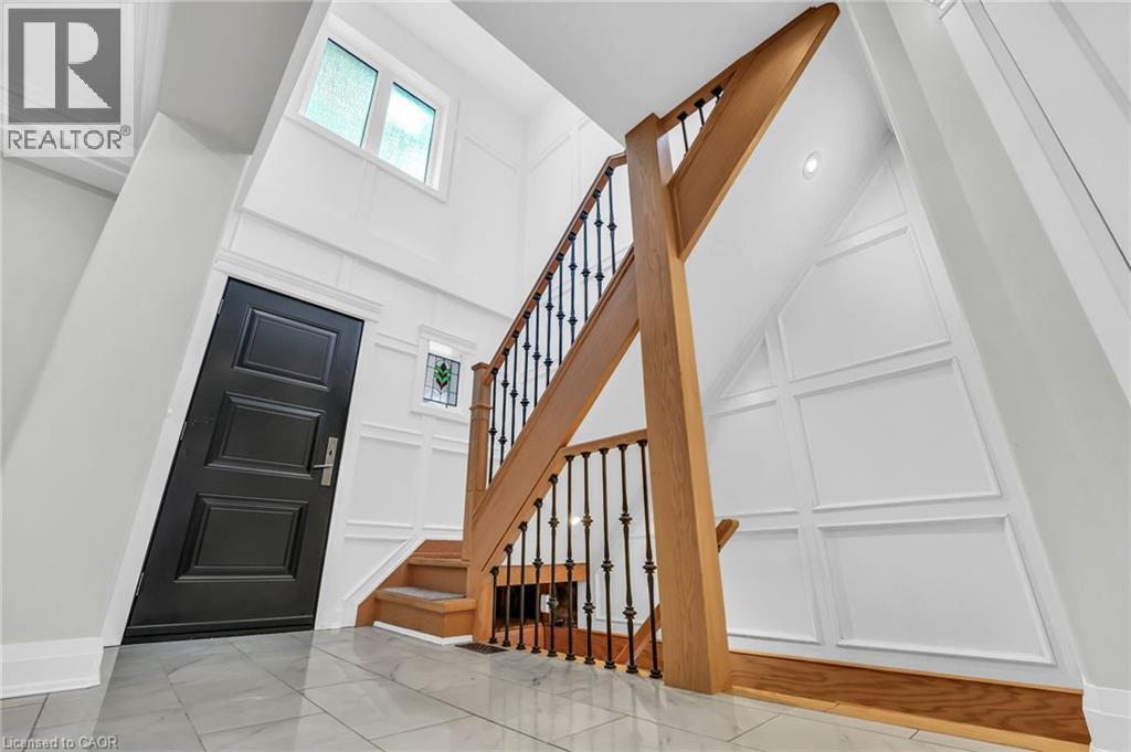 Two-story foyer featuring a wood staircase with wrought iron balusters, white wainscoting paneling, and a black paneled entry door - 25 Park Street E, Hamilton, ON - Indoor Photo Showing Other Room