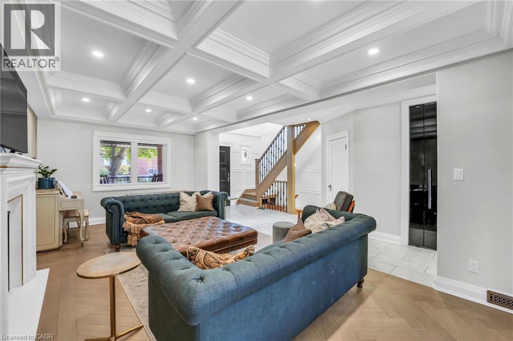 Open concept living space featuring a coffered ceiling with recessed lighting, herringbone wood-finish flooring, a white mantel, and a prominent staircase with dark iron balusters - 25 Park Street E, Hamilton, ON - Indoor