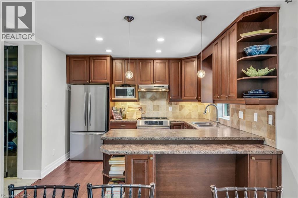 Kitchen featuring wood cabinetry, stainless steel appliances, speckled countertops, a tiled backsplash, and wood-finish flooring - 25 Park Street E, Hamilton, ON - Indoor Photo Showing Kitchen With Double Sink
