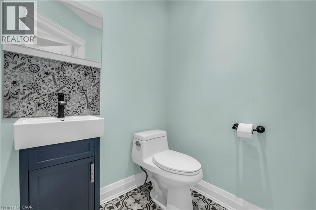 Modern powder room featuring a wall-mounted rectangular mirror, decorative tile backsplash, and a contemporary vanity with a vessel sink and matte black faucet - 25 Park Street E, Hamilton, ON - Indoor Photo Showing Bathroom