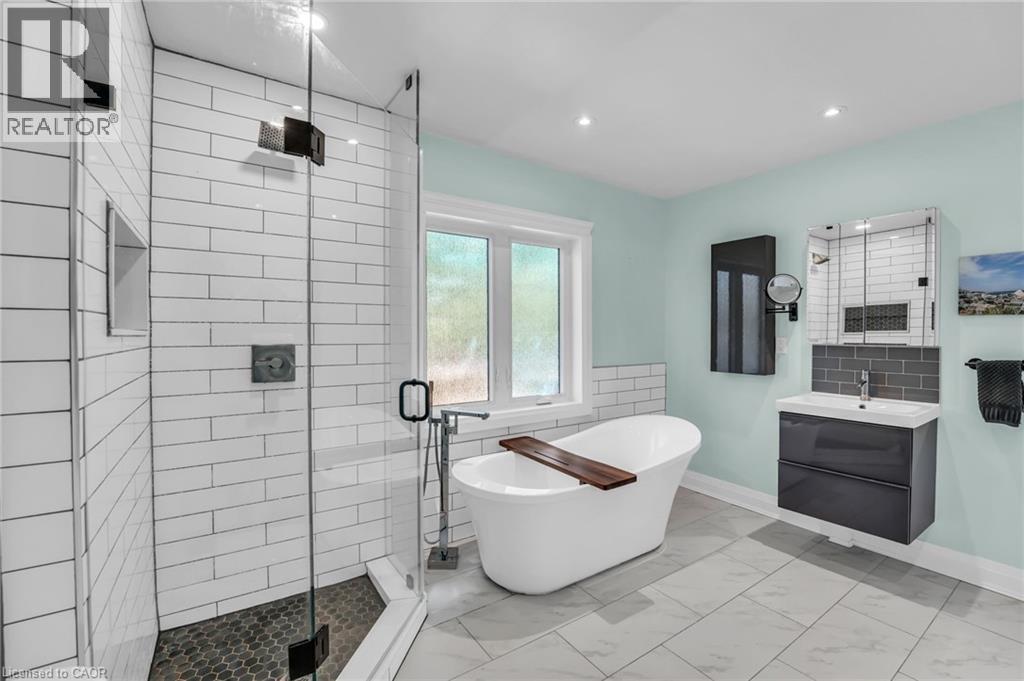 Bathroom featuring a glass-enclosed shower with white subway tile, a freestanding soaking tub, a floating vanity with an integrated sink, a mirrored medicine cabinet, and large-format tile flooring - 25 Park Street E, Hamilton, ON - Indoor Photo Showing Bathroom