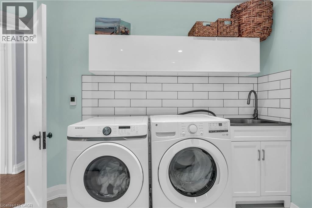 Dedicated laundry area featuring front-loading appliances, white subway tile backsplash, and a utility sink with a black faucet - 25 Park Street E, Hamilton, ON - Indoor Photo Showing Laundry Room