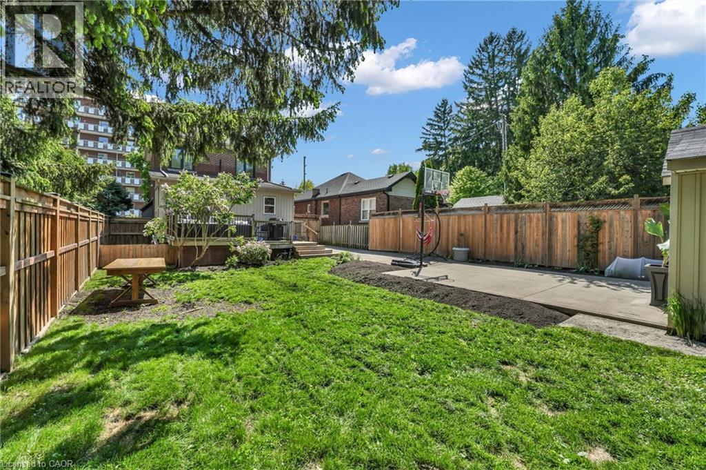 Expansive backyard featuring a large grass lawn, privacy fencing, a concrete patio area, a raised wood deck, and mature perimeter trees - 25 Park Street E, Hamilton, ON - Outdoor With Backyard