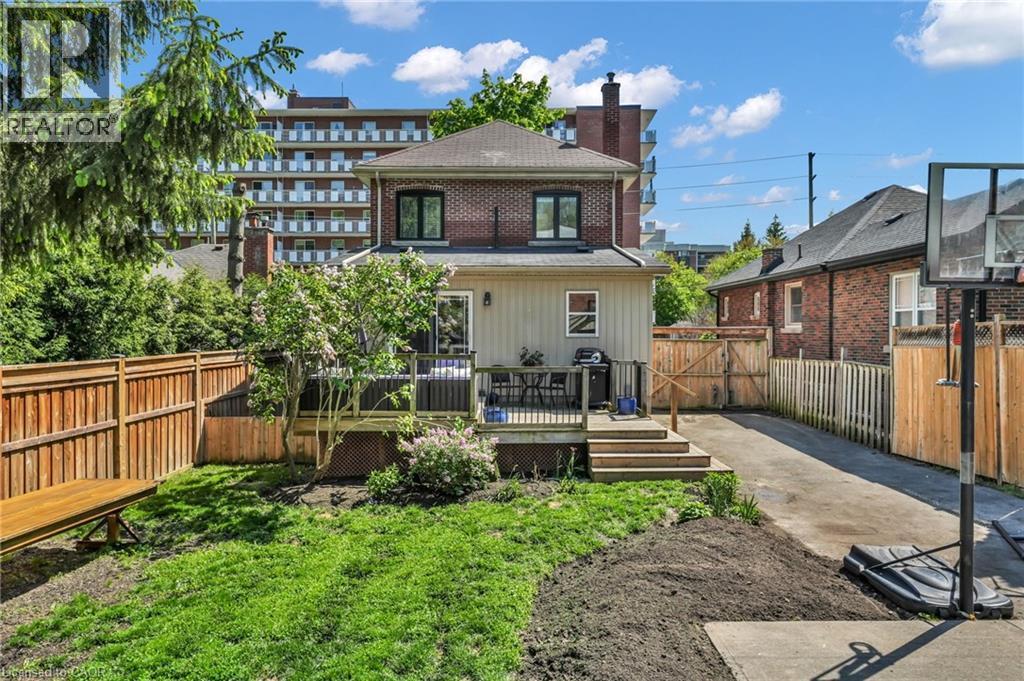 Rear exterior featuring a wood-deck patio with steps to a grass yard, a concrete driveway, and mature landscaping - 25 Park Street E, Hamilton, ON - Outdoor