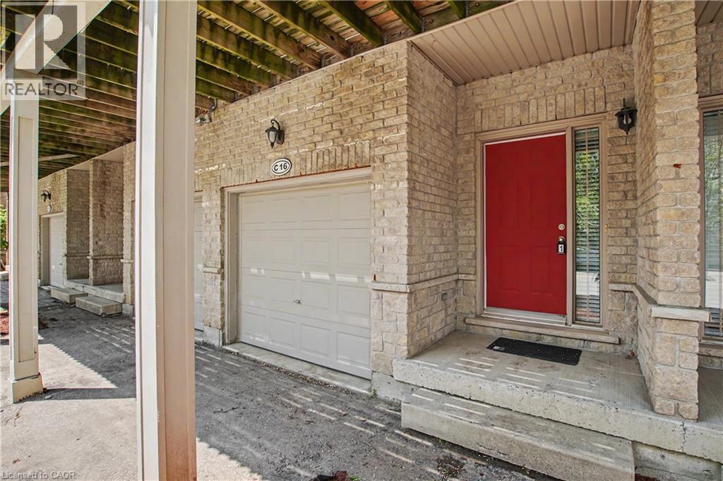 Front exterior featuring a vibrant red entry door, stone brick facade, and an integrated garage - 619 Wild Ginger Avenue Unit# C15 & #C16, Waterloo, ON - Outdoor With Exterior