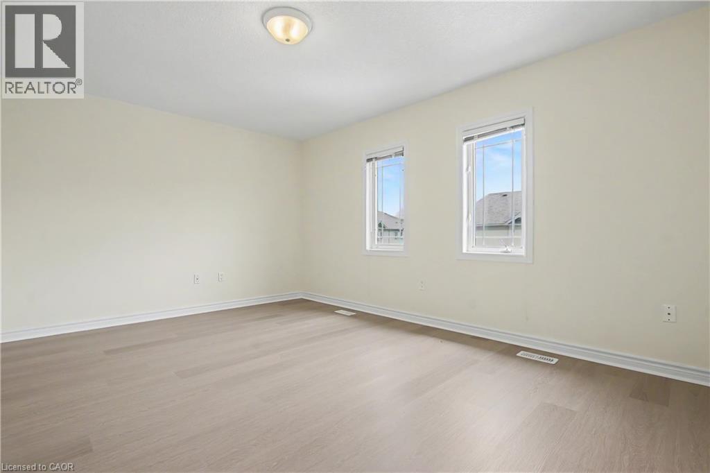 Spacious room featuring light-toned walls, wood-finish flooring, two large windows, a ceiling-mounted light fixture, and white baseboards - 619 Wild Ginger Avenue Unit# C15, Waterloo, ON - Indoor Photo Showing Other Room
