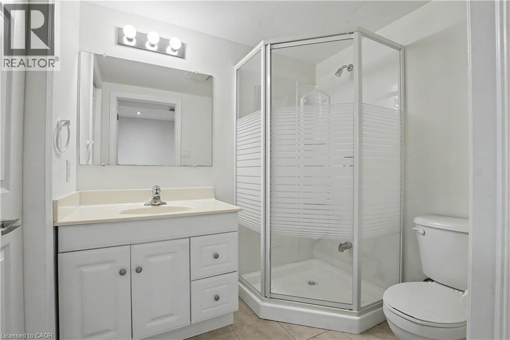 Bathroom featuring a corner shower with frosted glass, a single vanity with a light-colored countertop, white cabinetry, a wall-mounted mirror, and a three-light fixture - 619 Wild Ginger Avenue Unit# C15, Waterloo, ON - Indoor Photo Showing Bathroom