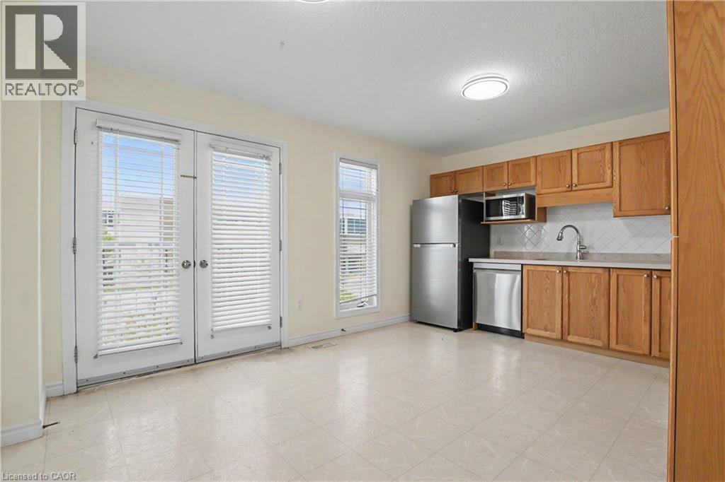 Combined kitchen and living area featuring a full suite of stainless steel appliances, light wood cabinetry, and a white tile backsplash - 619 Wild Ginger Avenue Unit# C15, Waterloo, ON - Indoor Photo Showing Kitchen