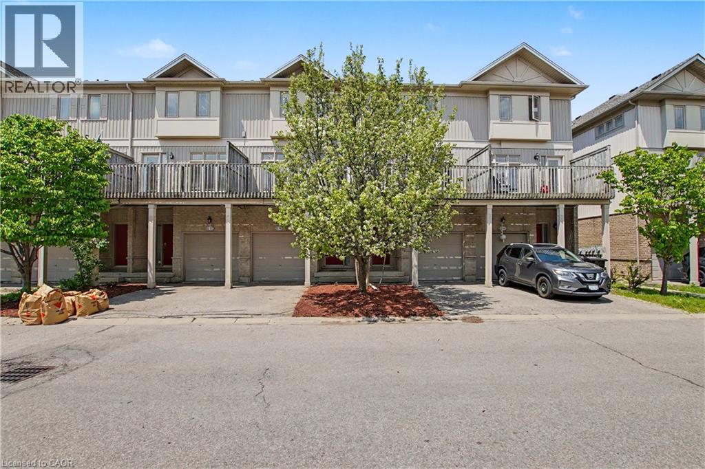 Multi-level townhouse exterior featuring light-colored siding, multiple balconies with wood railings, and individual garage access - 619 Wild Ginger Avenue Unit# C16, Waterloo, ON - Outdoor