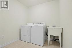 Dedicated laundry area featuring a utility sink with a chrome faucet, light-toned walls, and patterned tile flooring -