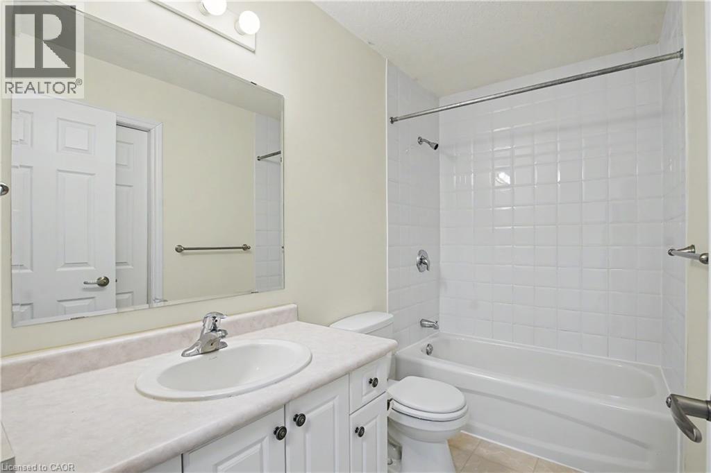 Bathroom featuring a white vanity with an integrated sink, a large wall-mounted mirror, overhead vanity lighting, a toilet, and a bathtub with white subway tile surround - 619 Wild Ginger Avenue Unit# C16, Waterloo, ON - Indoor Photo Showing Bathroom
