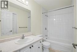 Bathroom featuring a white vanity with an integrated sink, a large wall-mounted mirror, overhead vanity lighting, a toilet, and a bathtub with white subway tile surround -