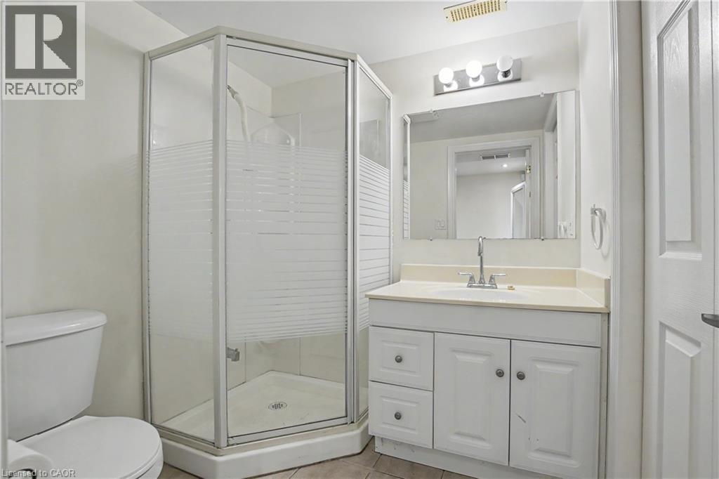 Contemporary bathroom featuring a corner shower with frosted glass enclosure, a white vanity with paneling, a countertop with integrated sink, a rectangular mirror, and overhead vanity lighting - 619 Wild Ginger Avenue Unit# C16, Waterloo, ON - Indoor Photo Showing Bathroom