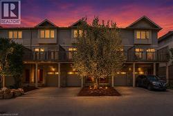 Contemporary townhome exterior featuring an elevated deck with wood railing, individual garage bays, and dedicated driveways -