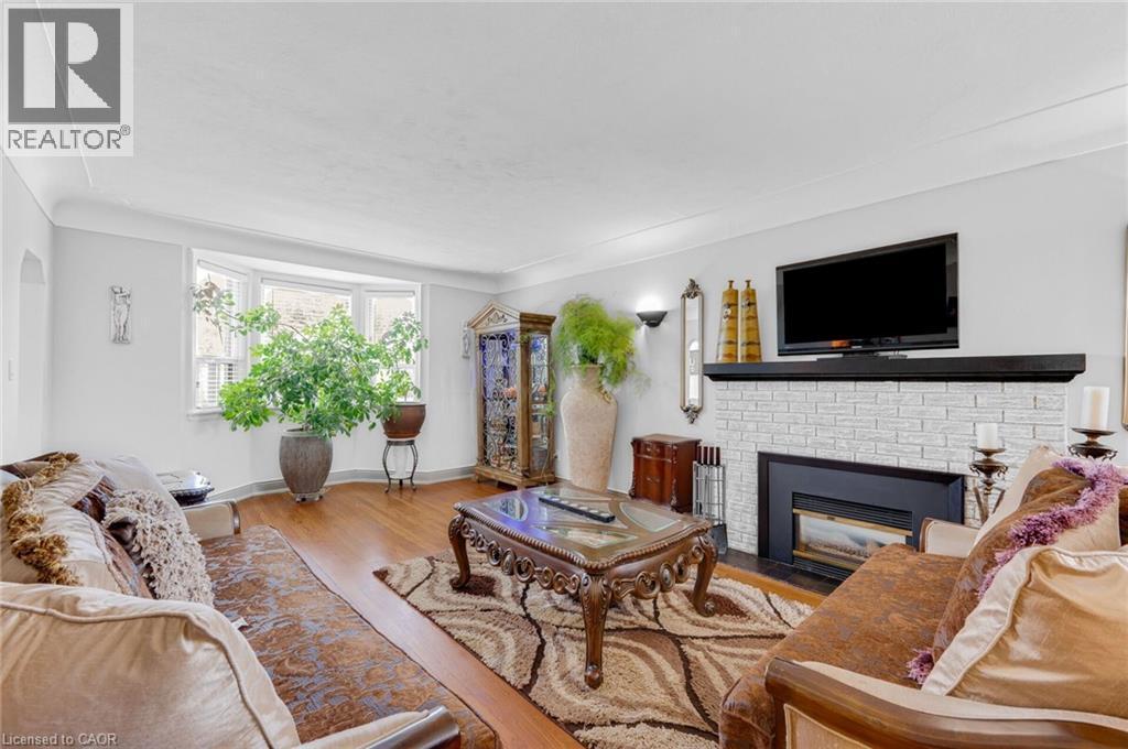 Living area featuring a bay window, hardwood flooring, and a fireplace with white brick surround and dark mantel - 1 Galbraith Drive, Hamilton, ON - Indoor Photo Showing Living Room With Fireplace