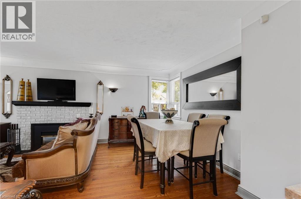 Open-concept living and dining area featuring rich wood-finish flooring, a white brick fireplace with a black mantel, and crown molding - 1 Galbraith Drive, Hamilton, ON - Indoor Photo Showing Dining Room With Fireplace
