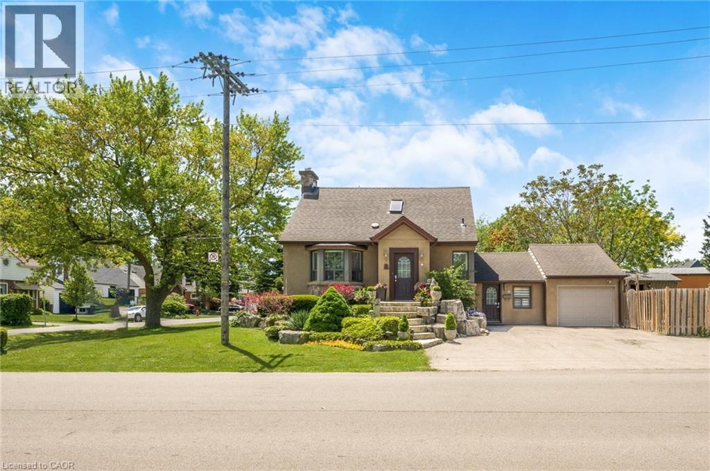Stucco exterior residence featuring a detached single-car garage, mature front yard landscaping with tiered stone elements, and a paved driveway - 1 Galbraith Drive, Hamilton, ON - Outdoor With Facade
