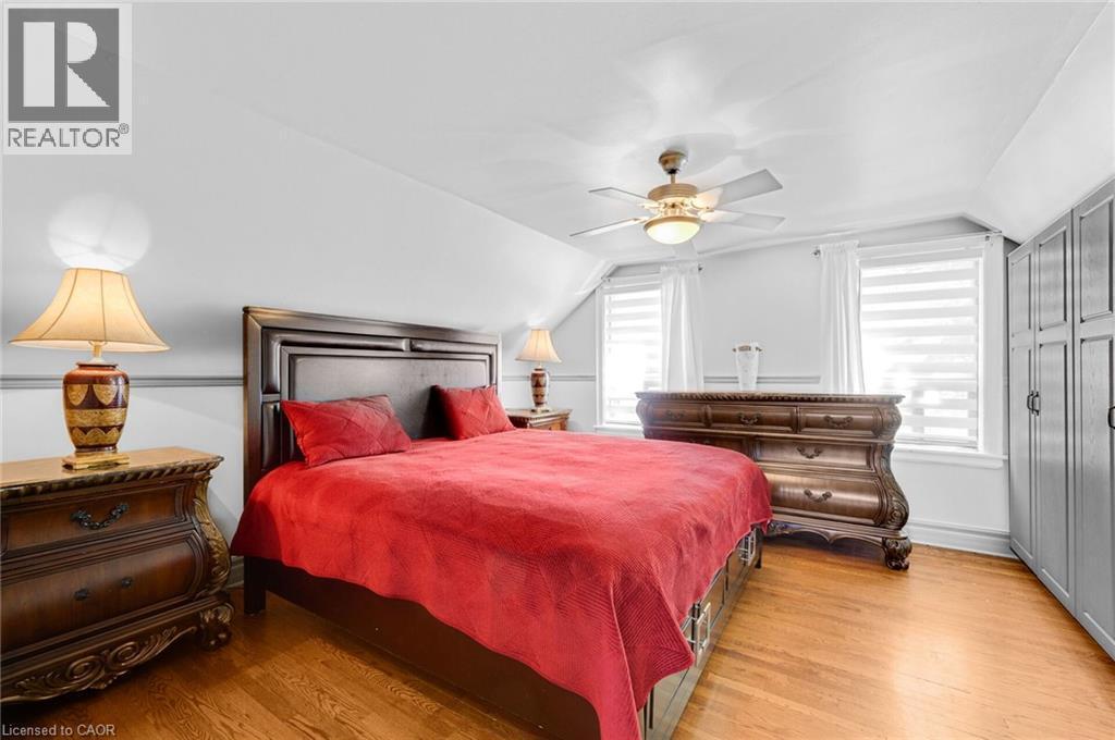 Hardwood flooring featuring an overhead fan with integrated lighting, two windows with horizontal blinds, and built-in cabinetry with panel detailing - 1 Galbraith Drive, Hamilton, ON - Indoor Photo Showing Bedroom