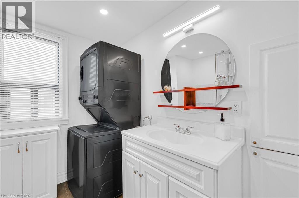 Laundry area featuring a stacked washer and dryer, white vanity with integrated sink, circular mirror with accent shelving, and recessed lighting - 1 Galbraith Drive, Hamilton, ON - Indoor Photo Showing Laundry Room