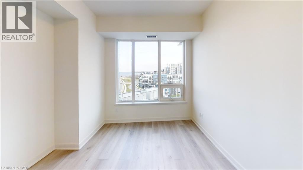 Spacious interior featuring a large window, light wood-finish flooring, white baseboards, and neutral wall finishes - 385 Winston Road Unit# 709, Grimsby, ON - Indoor Photo Showing Other Room