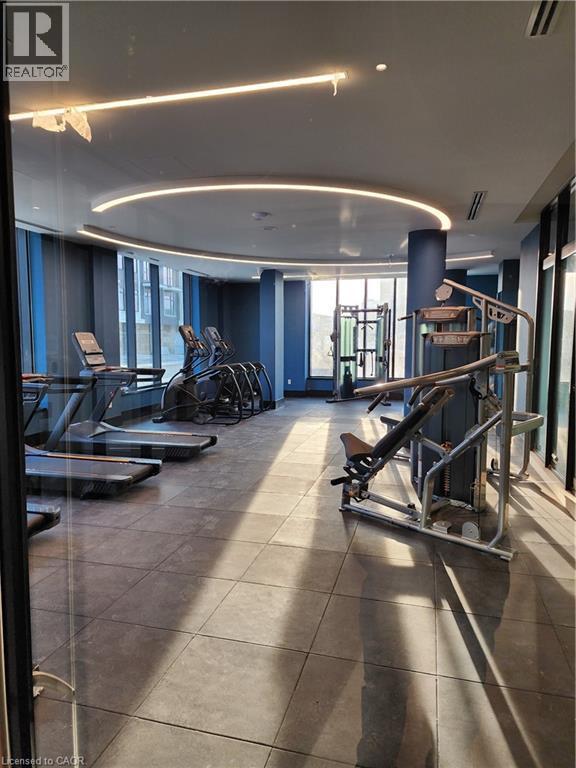 Fitness center with large format tile flooring, curved ceiling lighting, expansive windows, and a comprehensive selection of exercise equipment - 385 Winston Road Unit# 709, Grimsby, ON - Indoor Photo Showing Gym Room