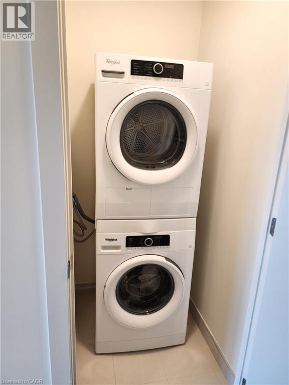Stackable washer and dryer unit in a dedicated laundry alcove with tile flooring - 385 Winston Road Unit# 709, Grimsby, ON - Indoor Photo Showing Laundry Room