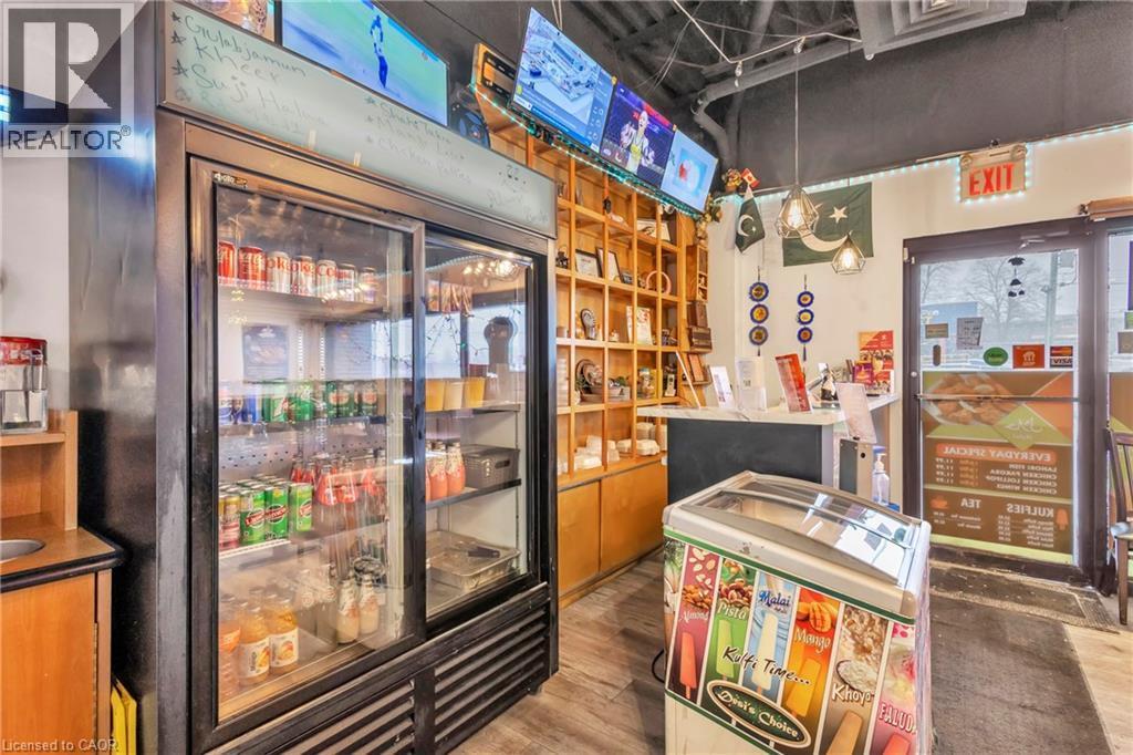 Commercial space featuring a large glass-front refrigeration unit, wood-finish flooring, recessed lighting, wall-mounted display shelving, and glass entry doors - 402 King Street N, Waterloo, ON