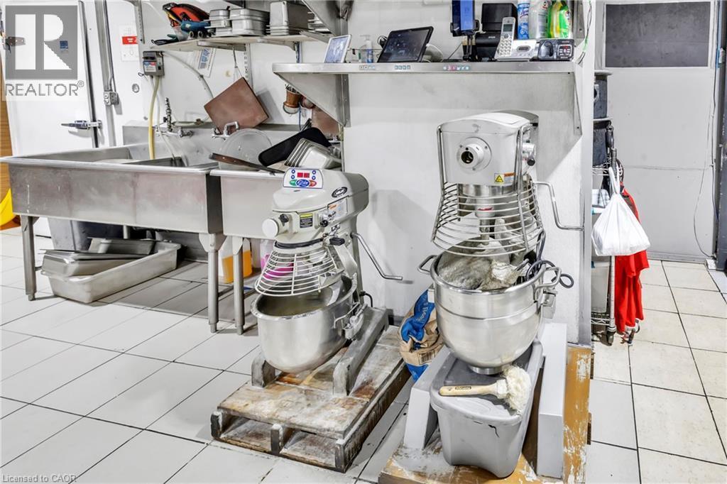 Commercial kitchen space featuring white tiled flooring, stainless steel three-compartment sink, stainless steel shelving, and a white commercial refrigeration unit - 402 King Street N, Waterloo, ON