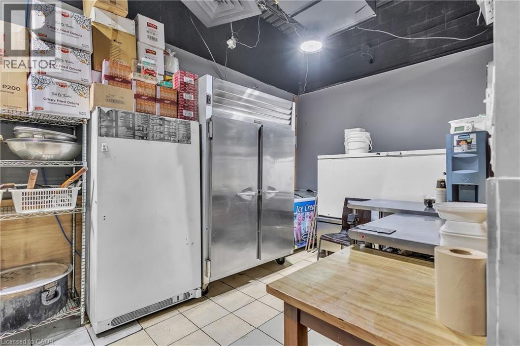 Commercial kitchen space featuring stainless steel refrigeration units, tile flooring, and a wooden work table - 402 King Street N, Waterloo, ON