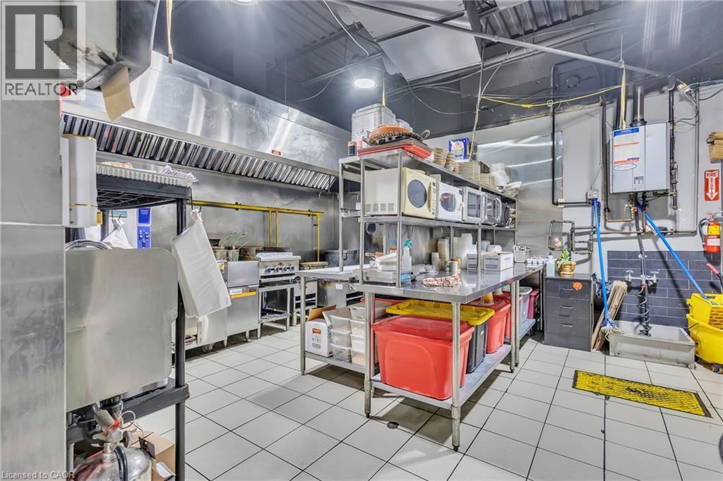 Commercial kitchen featuring stainless steel equipment, tiled flooring, exposed ceiling with ductwork, and wall-mounted water heaters - 402 King Street N, Waterloo, ON