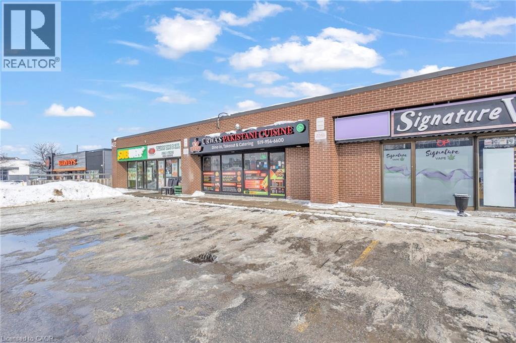 Commercial brick storefronts featuring multiple retail units, individual signage, and ample front parking - 402 King Street N, Waterloo, ON