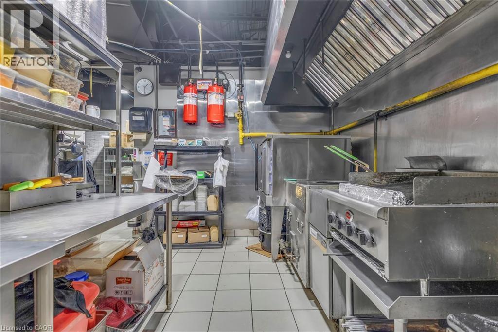 Professional kitchen space featuring commercial-grade stainless steel equipment, including a range with griddle, a large exhaust hood, and multiple work tables - 402 King Street N, Waterloo, ON