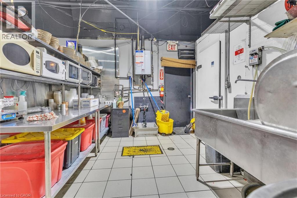 Commercial-grade kitchen space featuring white square tile flooring, stainless steel work surfaces, and a large commercial sink - 402 King Street N, Waterloo, ON
