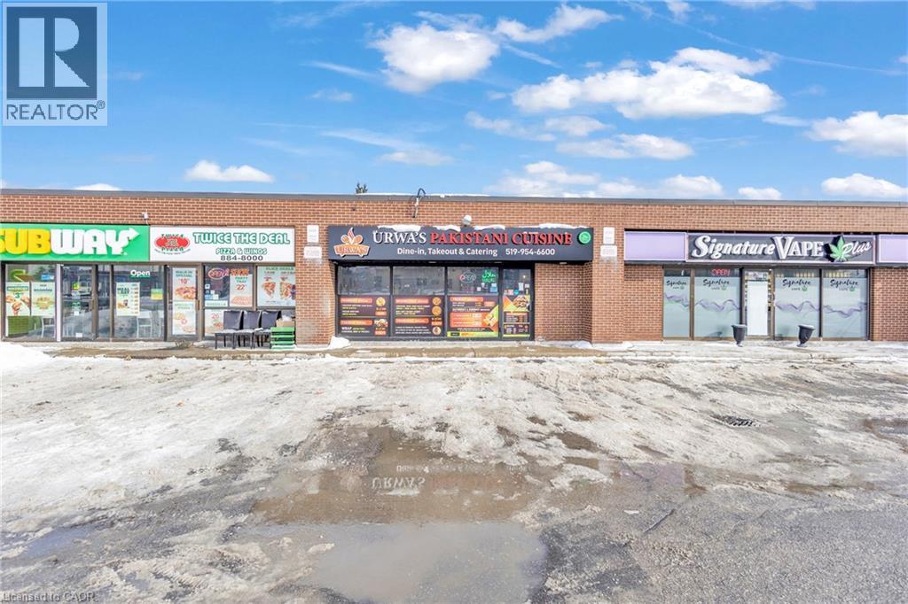 Commercial storefront featuring brick facade, multiple display windows, prominent signage, and a paved parking area - 402 King Street N, Waterloo, ON