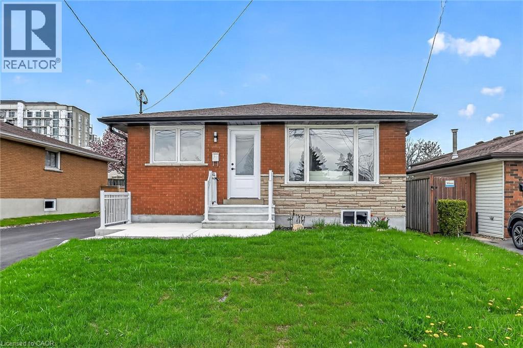Brick facade home featuring a stone veneer accent, white trim windows, and a front entry door with a storm door - 74 Victor Boulevard, Hamilton, ON - Outdoor