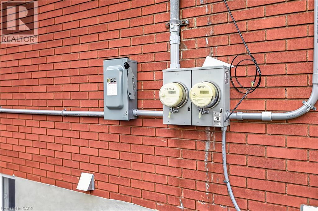 Red brick exterior wall featuring gray conduit piping, two utility meters, and a separate electrical service box - 74 Victor Boulevard, Hamilton, ON - Indoor Photo Showing Other Room