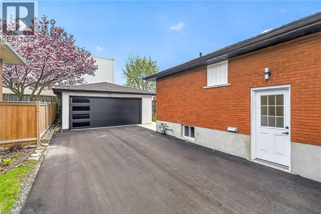 Detached garage featuring a contemporary black door with horizontal window inserts, white siding, and a shingled roof - 74 Victor Boulevard, Hamilton, ON - Outdoor With Exterior