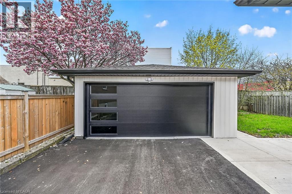 Detached garage featuring a modern black garage door with horizontal window inserts, white vertical siding, and a dark shingled roof - 74 Victor Boulevard, Hamilton, ON - Outdoor