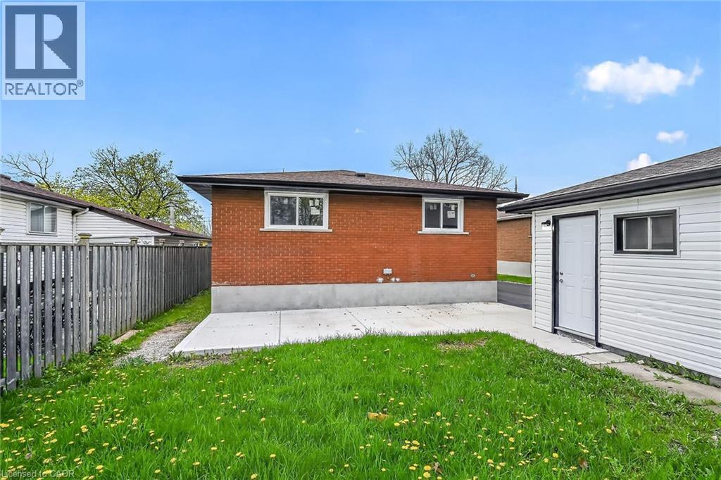 Rear exterior featuring red brick construction, a concrete patio, and a separate white-sided auxiliary structure with a dark roof - 74 Victor Boulevard, Hamilton, ON - Outdoor With Exterior