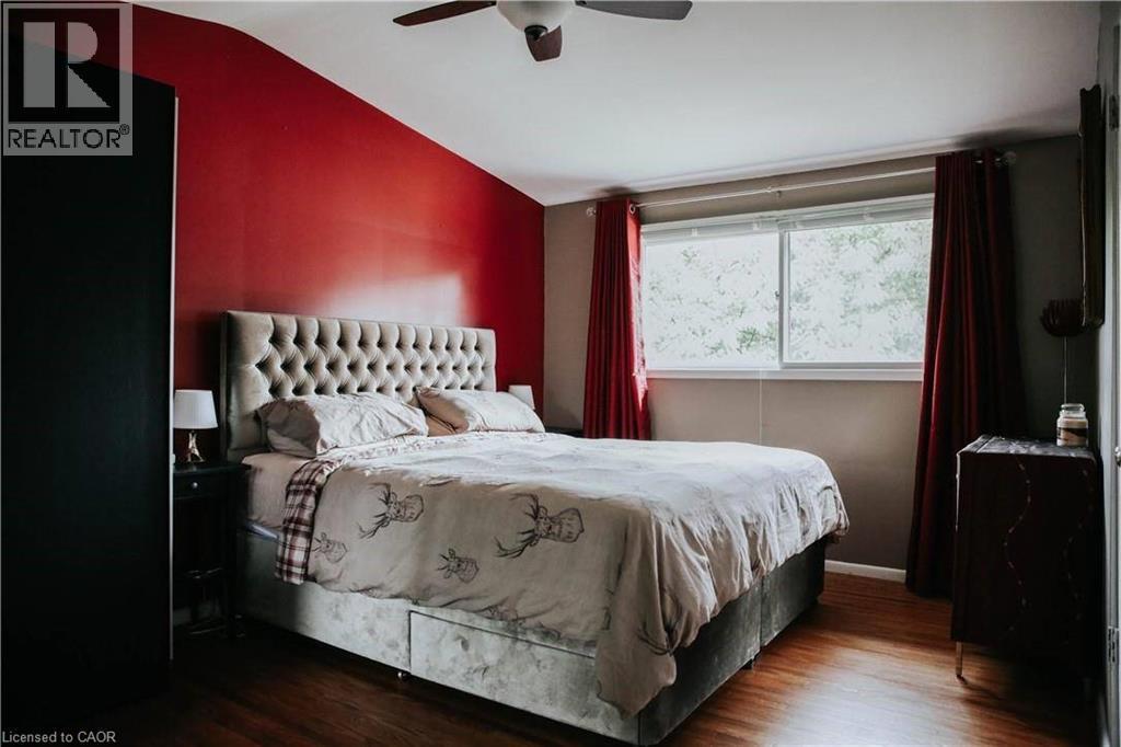 Bedroom featuring wood-finish flooring, a ceiling fan, and a prominent red accent wall - 1 Vera Court, Hamilton, ON - Indoor Photo Showing Bedroom