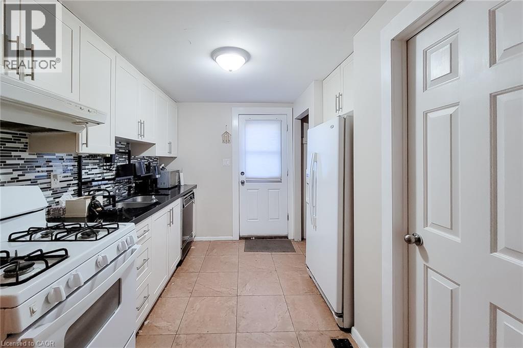 Galley kitchen featuring white cabinetry, a mosaic tile backsplash, black countertops, and a full-size refrigerator - 1 Vera Court, Hamilton, ON - Indoor Photo Showing Kitchen With Double Sink