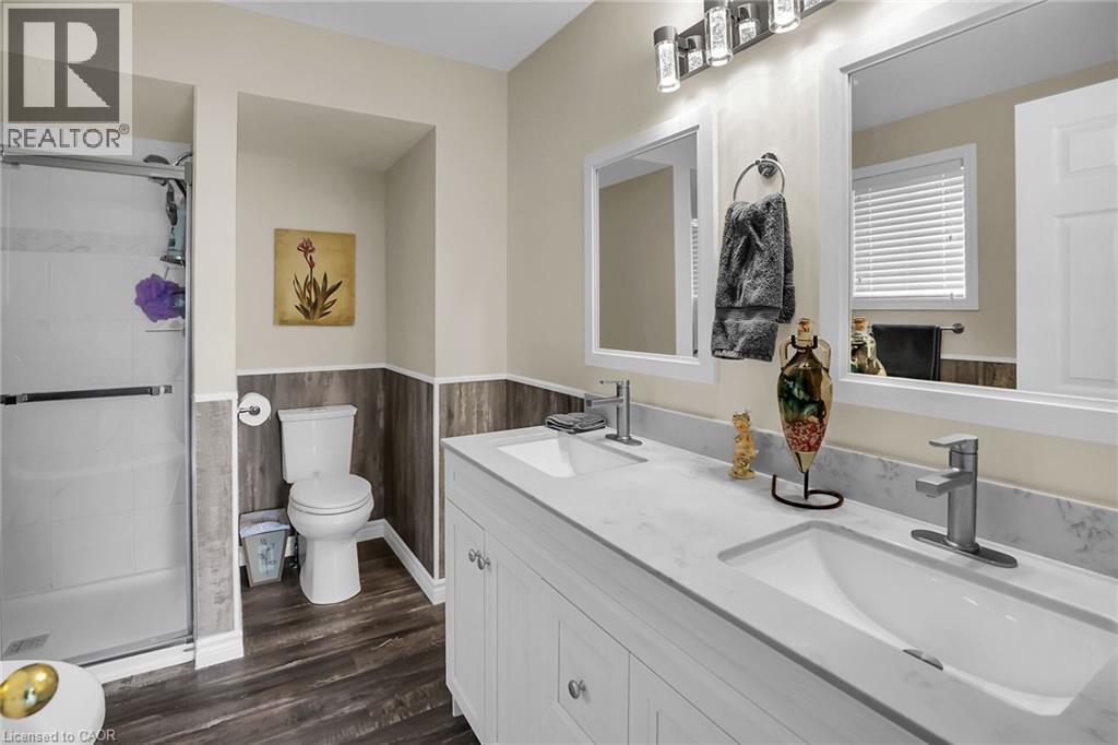 Bathroom featuring wainscoting, double vanity, a stall shower, and wood finished floors - 4432 Dennis Avenue, Beamsville, ON - Indoor Photo Showing Bathroom