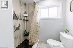 Shower with marble-look tile surround and black hexagonal tile flooring, featuring a window with white trim and a white toilet -